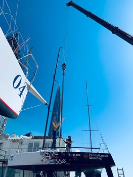 Russia, St.Petersburg, 26 May 2020: Port Hercules, the big industrial crane lifts the sailboat and floats it, the beginning of a season of sailing, a skyscraper on a background, sailboat is groundless, sunny weather