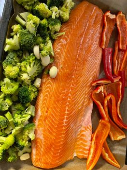 A large piece of red fish fillet lies on the prostena, vegetables ready to be locked, broccoli, red sweet pepper. High quality photo