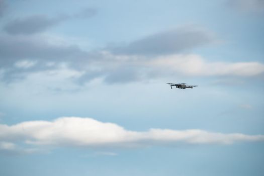 The flying soaring drone in the sky, the blue sky with white clouds, sunny weather, Turning propellers, nobody. High quality photo