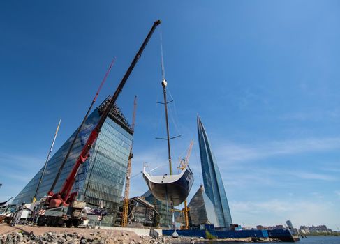 Russia, St.Petersburg, 26 May 2020: Port Hercules, the big industrial crane lifts the sailboat and floats it, the beginning of a season of sailing, a skyscraper on a background, sailboat is groundless, sunny weather