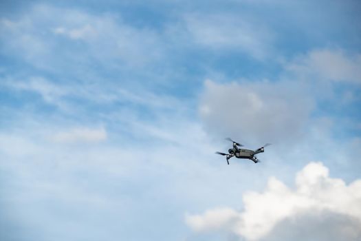 The flying soaring drone in the sky, the blue sky with white clouds, sunny weather, Turning propellers, nobody. High quality photo