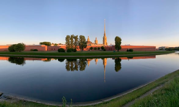 Russia, St.Petersburg, The picturesque reflection of the Peter and Paul Fortress in the kronverksky passage on a sunset, Quiet water, blue sky, wall of fortress of orange color