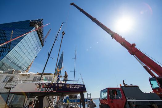 Russia, St.Petersburg, 26 May 2020: Port Hercules, the big industrial crane lifts the sailboat and floats it, the beginning of a season of sailing, a skyscraper on a background, sailboat is groundless, sunny weather