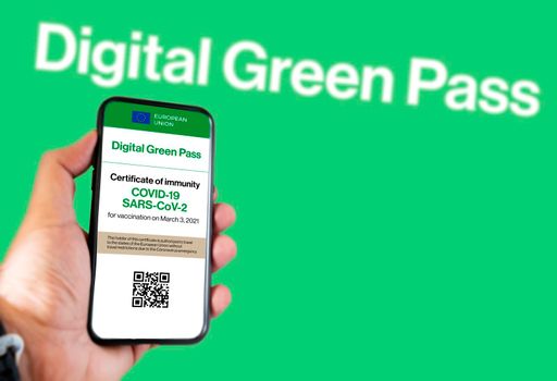 The digital green pass of the european union with the QR code on the screen of a mobile held by a hand with a blurred green background. Immunity from Covid