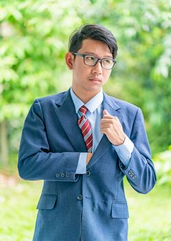 Young asian business men portrait in suit and wear eyeglasses standing outside in a park during sunny day