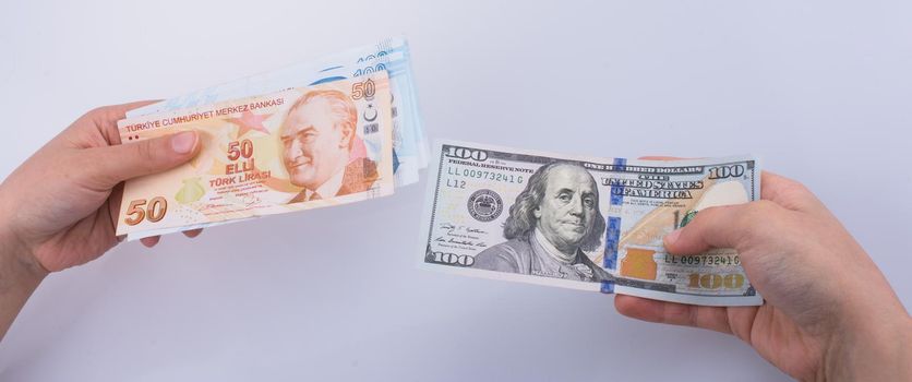 Hands holding American dollar banknotes and Turksh Lira banknotes side by side on white background