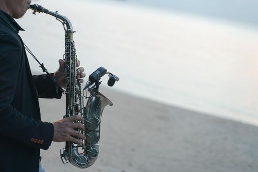 Musician man playing saxophone on the beach.