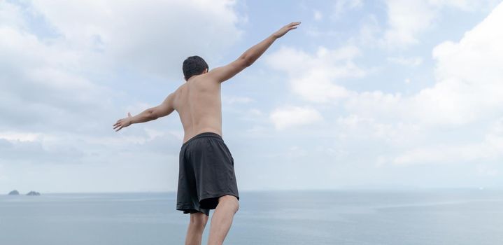 Back view of man opened hands with delight at the ocean and sky.