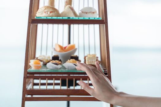 Woman hand with a set of luxury traditional afternoon tea with dessert served in bird cage.