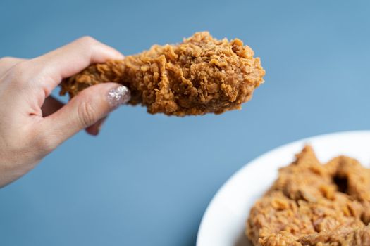 Hand holding drumsticks, crispy fried chicken in white plate on blue background.