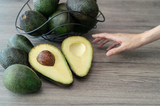 Woman hand with cut half, sliced fresh green avocado on brown wooden table. Fruits healthy food concept.