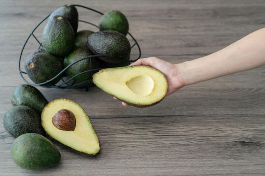 Woman hand holding cut half, sliced fresh green avocado on brown wooden table. Fruits healthy food concept.