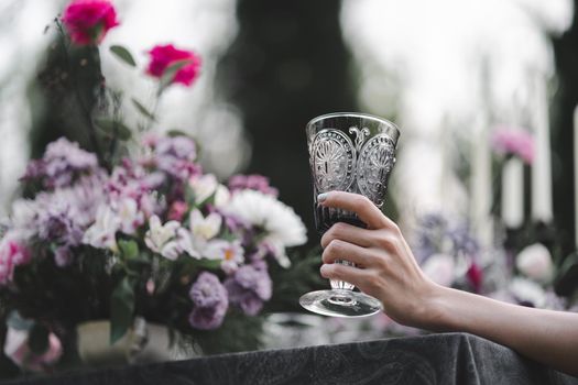 Glass of water in woman hand. Garden and flowers background.