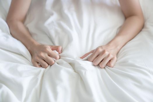 Woman hand grasping white sheet. Couple making love or having sex in bedroom.