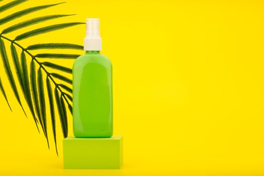 Spray for sun protection with sunscreen in green tube on podium against yellow background with palm leaf and copy space. High quality photo