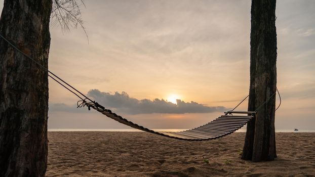 A wooden swing or cradle on the beach with beautiful cloud and sky.