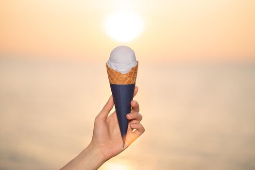 Scoop ice cream with a waffle cone in hand on the beach, sunset moment.