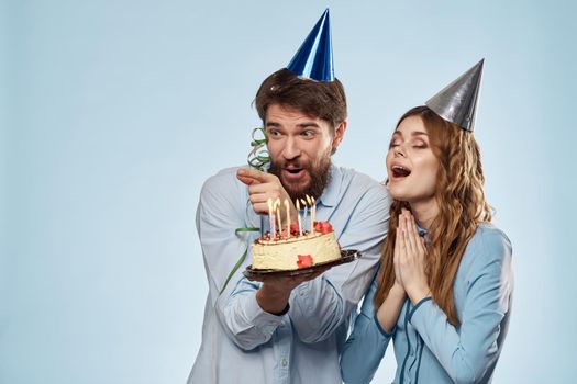 man and woman celebrate birthday with cake and in hats on blue background. High quality photo