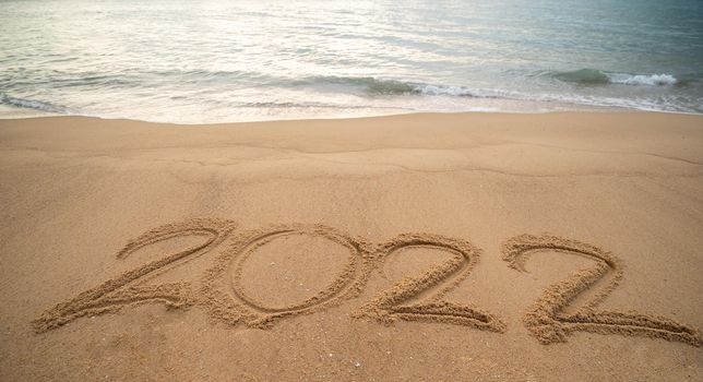 Handwriting year 2022 on sand and foam wave on beach.