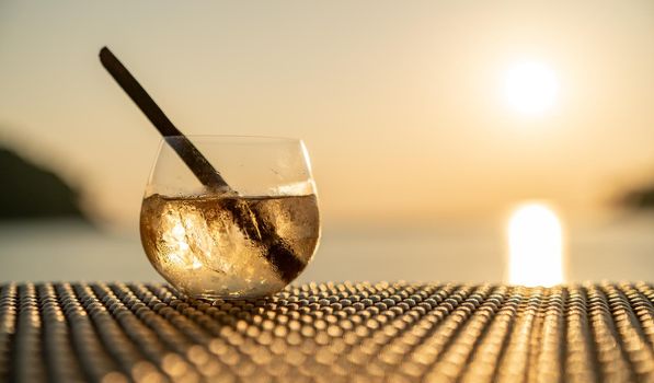 Ice cocktail glasses with cinnamon straws on wooden table over sea sunset.