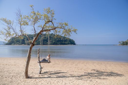 Woman sitting on a swing, on the beach.