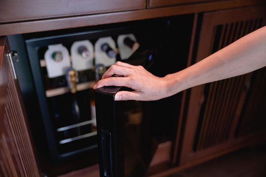 Woman hand open storing bottles of wine in fridge. Cooling and preserving wine.