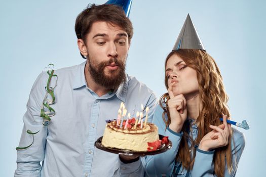 man and woman celebrate birthday with cake and in hats on blue background. High quality photo