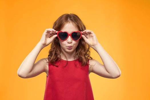 Girl in black glasses red dress childhood fun yellow background. High quality photo