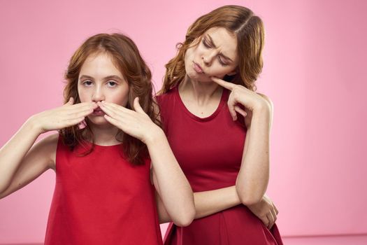 Mom and daughter in red dresses hugs fun grimace childhood joy pink background. High quality photo