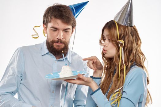 energetic man and woman with a cake and in hats celebrate a birthday on a light background. High quality photo