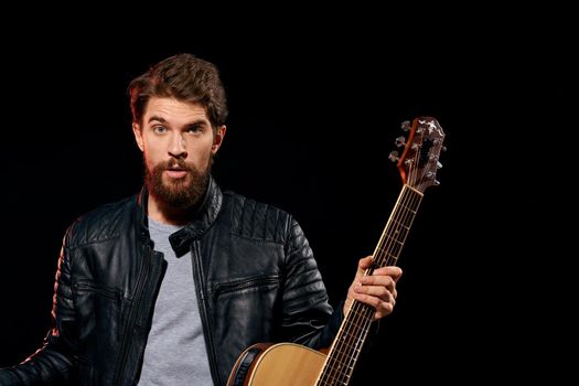 A man with a guitar in his hands leather jacket music performance rock star modern style dark background. High quality photo