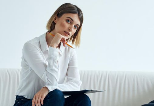 A woman sits on a sofa In a bright room in a shirt and papers . High quality photo