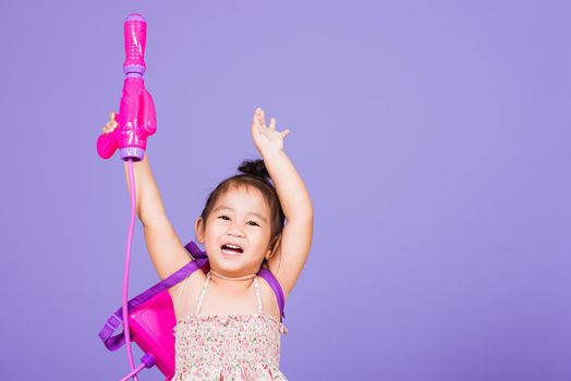 Happy Asian little girl holding plastic water gun, Thai child funny hold toy water pistol and smile, studio shot isolated on purple background, Thailand Songkran festival day national culture concept