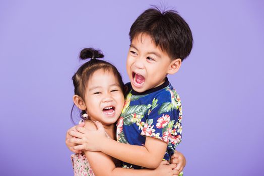 Asian Two happy funny little cute kids stand together in studio shot isolated on purple background, happy family brother and sister hugging each other feeling love (4 years old boy, 2 years old girl)