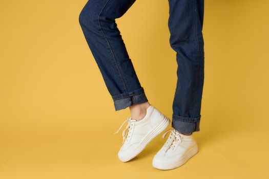 Womens legs jeans white sneakers fashion street style yellow background. High quality photo