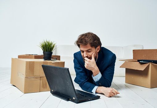A business man lies on the floor in front of a laptop, work with no unpacked things. High quality photo