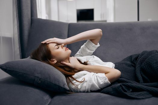 woman at home lies on the sofa covered with a blanket feeling unwell hand on face. High quality photo