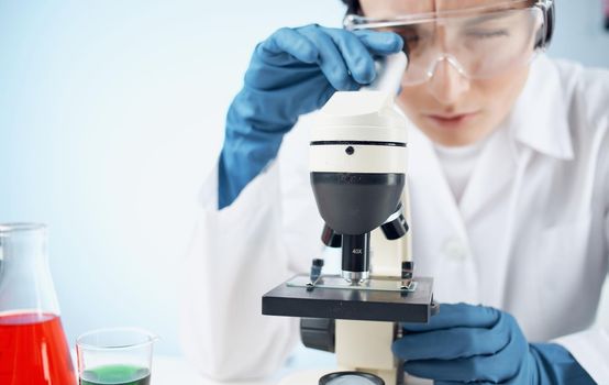 woman in a medical gown in blue gloves stands near the flask and biology chemical element vaccination. High quality photo