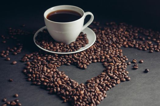 cup with a fragrant drink on a dark background heart of coffee beans white saucer. High quality photo