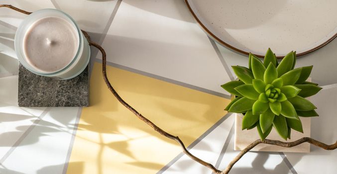 Home plant, candle on pastel yellow grey background. Cosy home with morning sun light, top view. Horizontal flat lay