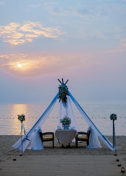 A loving couple shares a romantic dinner with candles, lanterns, and wine glasses at sea beach sand against wonderful sunset. Romantic dinner on the beach