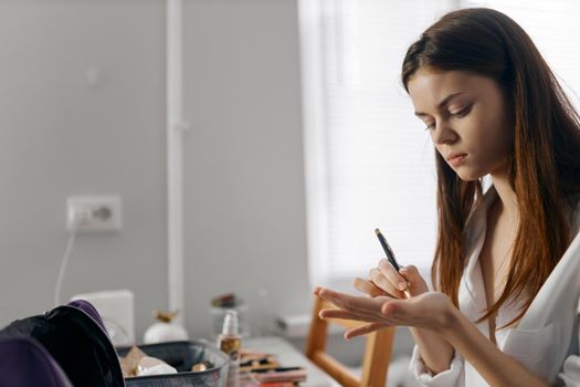 woman holding a pencil and sitting at the table cosmetics eyeliner portrait foundation. High quality photo