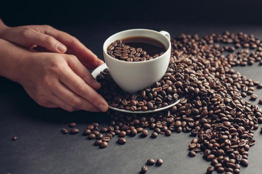 aromatic coffee beans on a gray table and hands near a cup with a drink. High quality photo