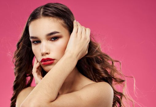 Sexy brunette with red lips on a pink background touch her hair with her hands. High quality photo