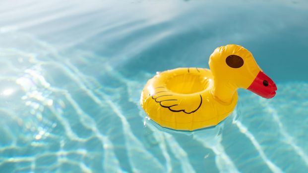 Cute yellow rubber duck floating on blue water in a pool.