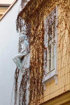 Prague, Czech Republic April 14, 2018. Sculpture of a girl sitting on the edge of the building's roof. Plants grow on the wall.