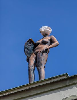 Prague, Czech Republic April 14, 2018. A sculpture of a naked girl standing on the edge of the roof of a building. Instead of a head, a lantern