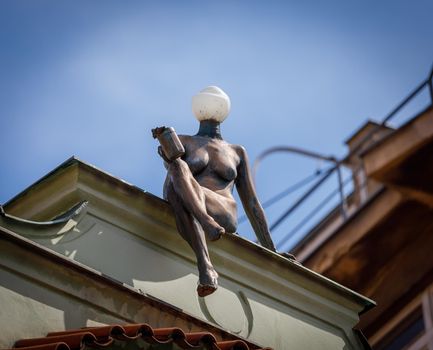 Prague, Czech Republic April 14, 2018. A sculpture of a naked girl sitting on the edge of the roof of a building. Instead of a head, a lantern