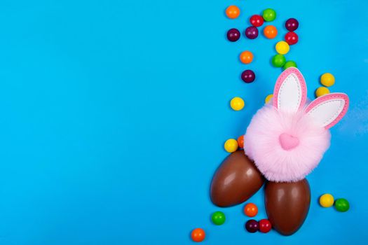 Easter concept, candy jelly beans, chocolate egg, pink rabbit head toy on a blue background. Place for text