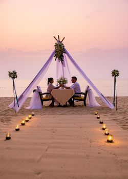 couple men and woman having romantic dinner with candle lights on the beach in Thailand, European men and Asian woman dinner on the beach Valentine concept. Romantic dinner on the beach